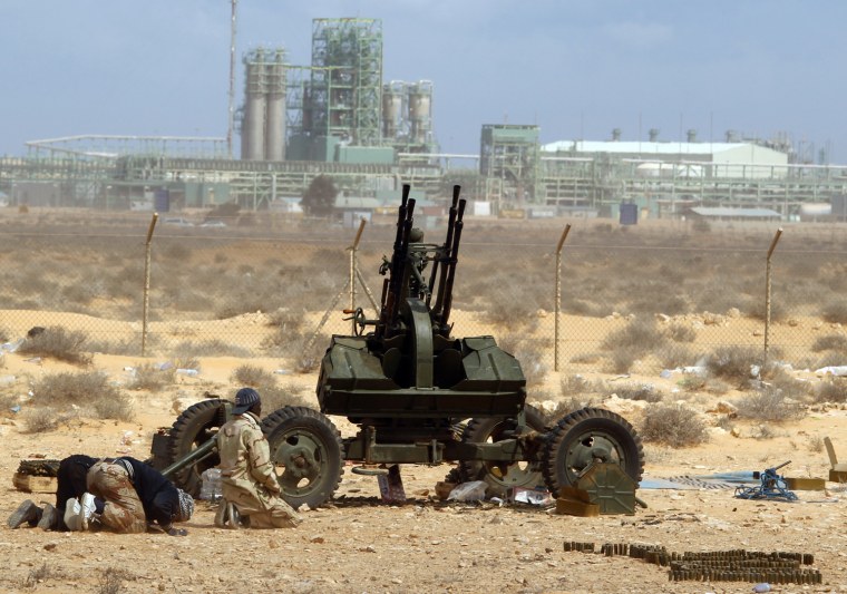 Image: Rebels pray in front of anti-aircraft gun in front of a refinery in Ras Lanuf